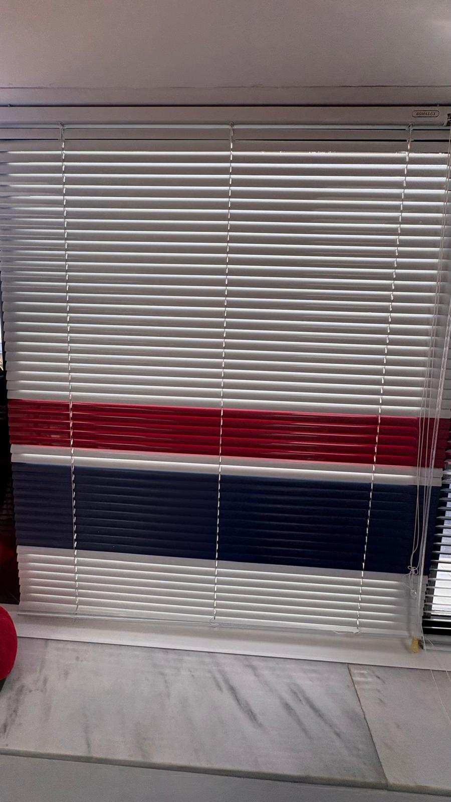 Persiana veneciana de aluminio con lamas de colores instalada en un ventanal